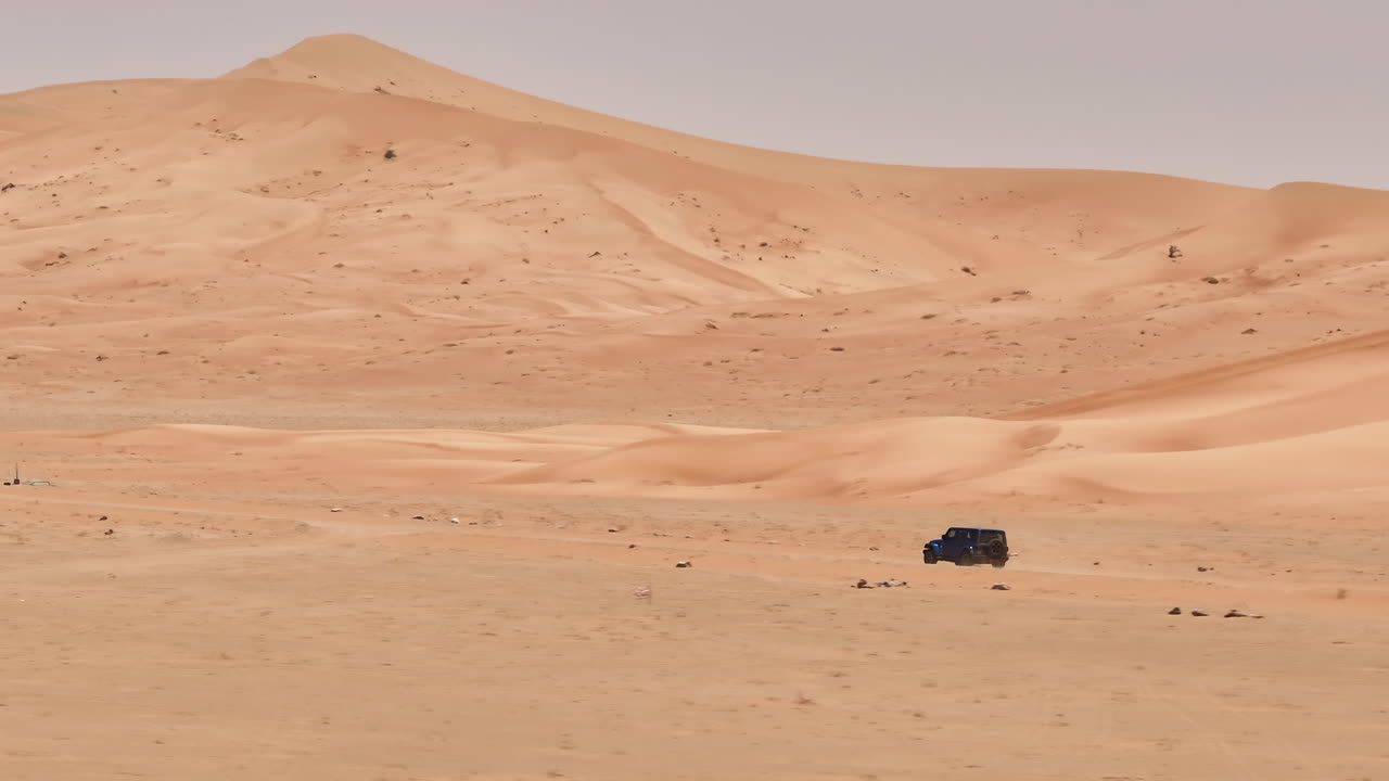 Desert landscape with a vehicle navigating the vast, empty expanse of Oman's Empty Quarters