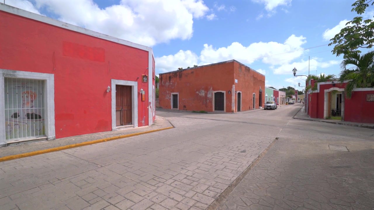 Ampia ripresa statica di colorati edifici coloniali rossi e color terracotta che costeggiano un tranquillo incrocio di strade acciottolate sotto un cielo soleggiato a Valladolid, Yucatan, Messico