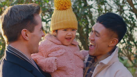 portrait of family with two dads on walk in winter countryside carrying daughter