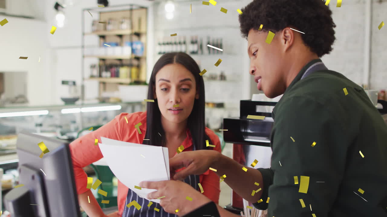 Coworkers reviewing marketing papers behind café counter, showcasing floating gold confetti