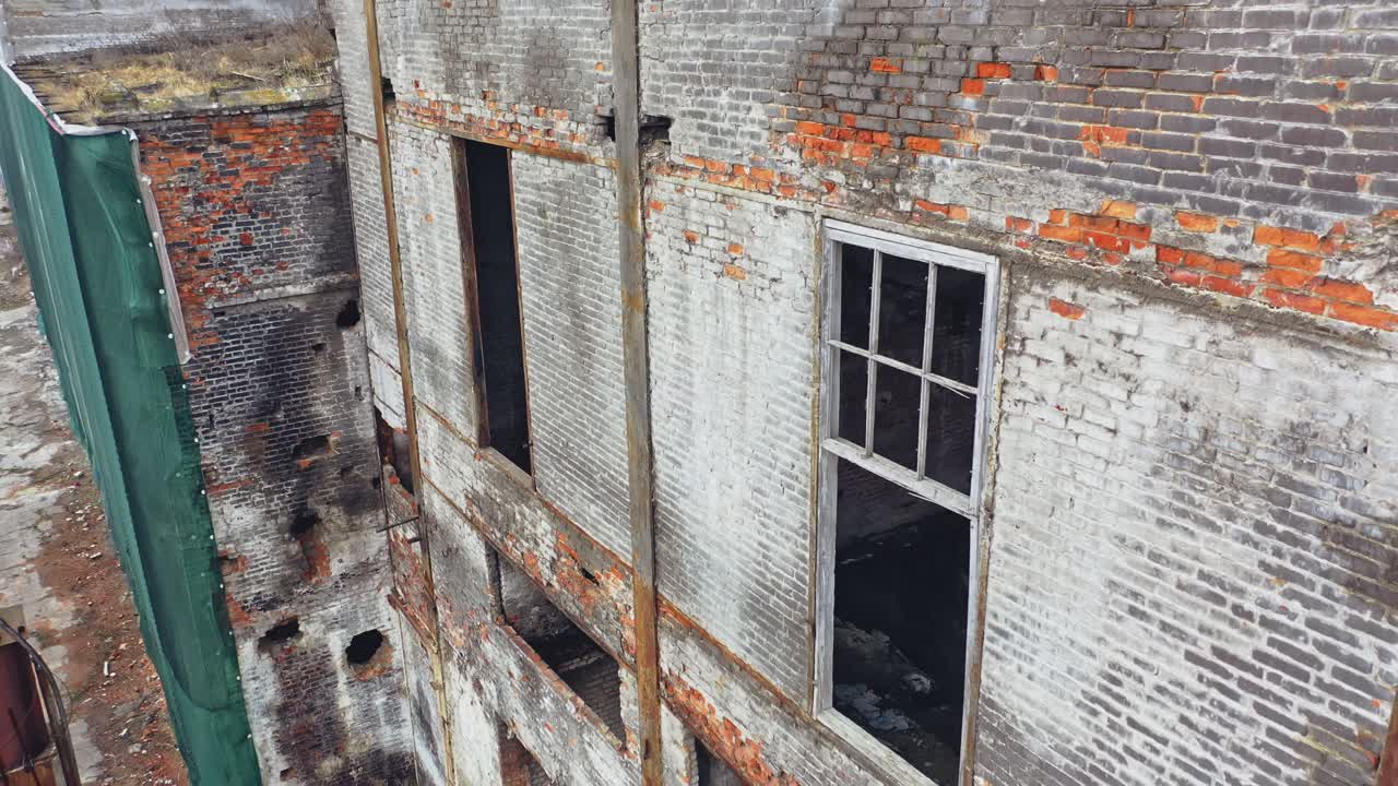 Damaged brick building without windows after the war. Close view of a destructed house with many holes in the wall. Camera moves top down