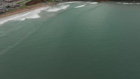 High-elevation-drone-view-over-hundreds-of-surfers-catching-waves-in-california