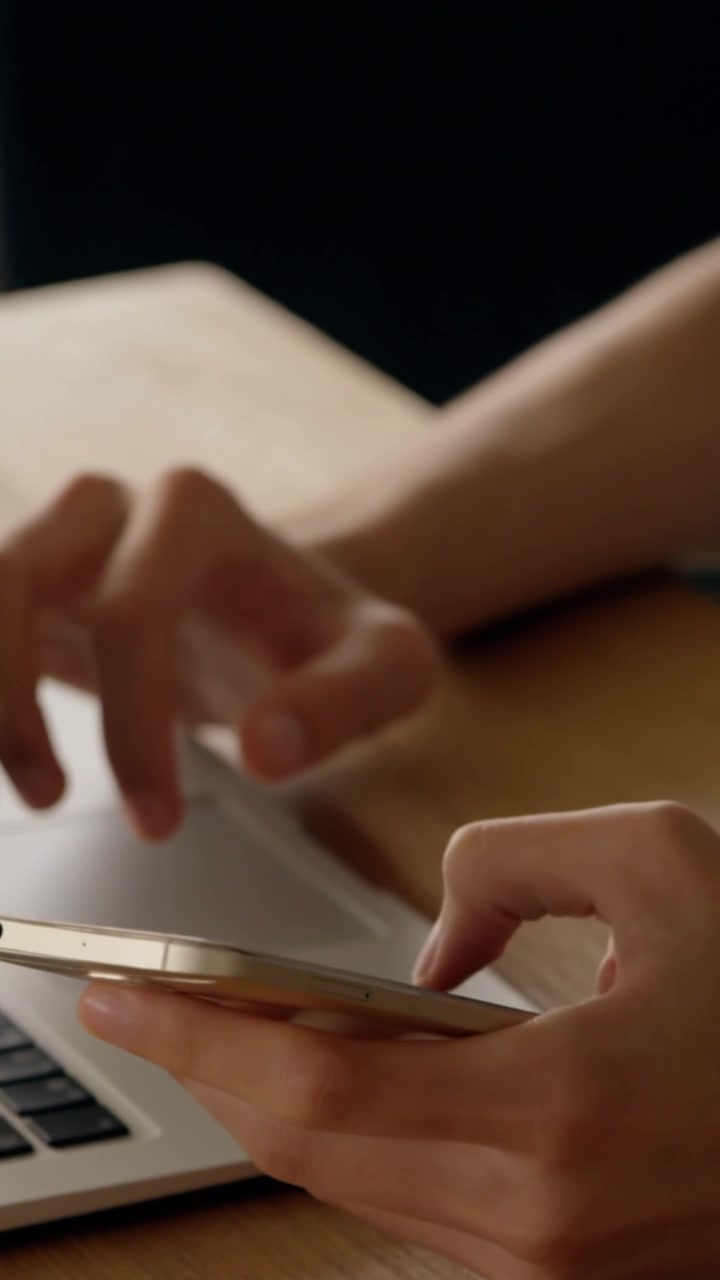 Midsection of man texting on smartphone and using laptop at desk
