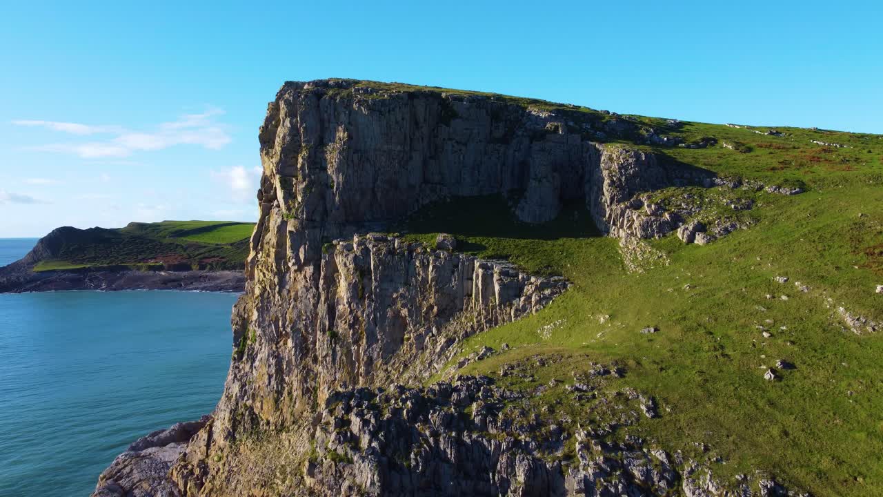 Rising Aerial Over Sheer Cliffs on Gower Coastline with Rocky Terrain and Grassy Paths. Natural Wales with Blue Sky and Ocean. Travel Nature Drone Clip