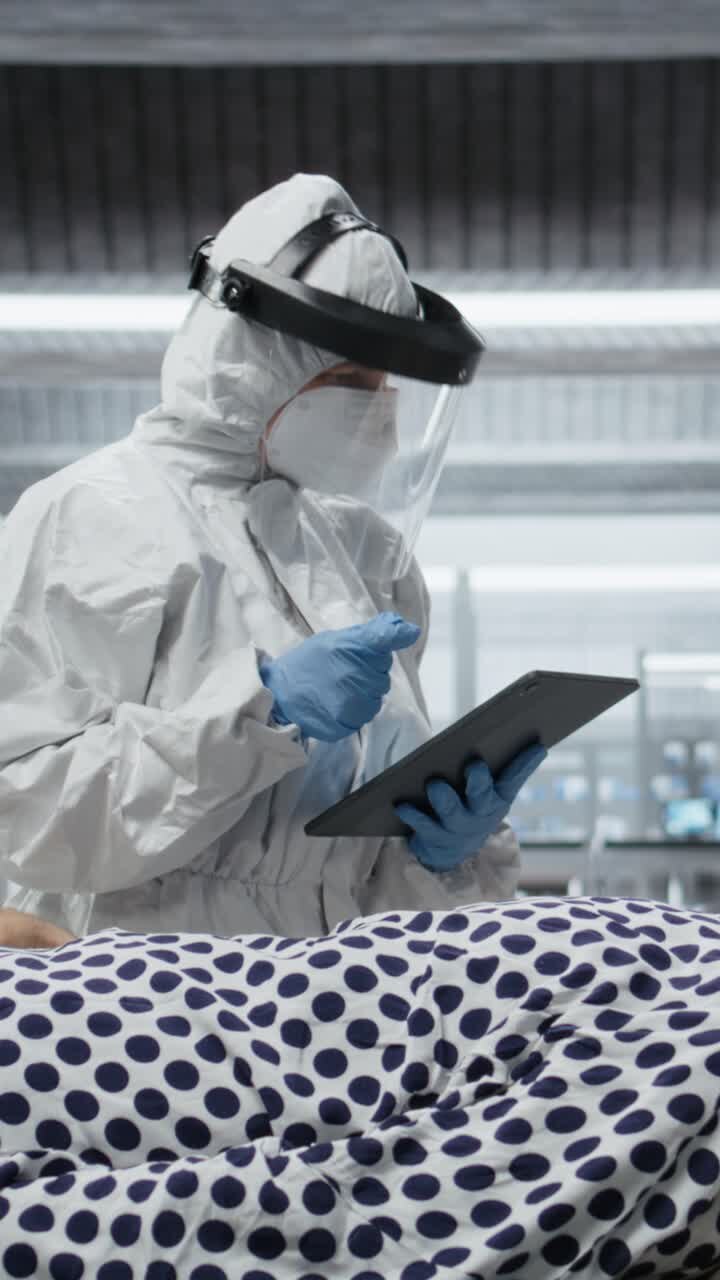 Video verticale: un medico in tuta protettiva e guanti visita un paziente in quarantena