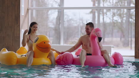 man and woman are resting in public swimming pool sitting on funny lifebuoy weekend in waterpark