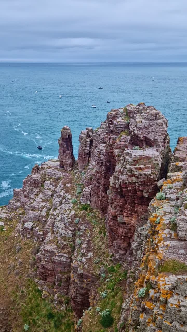 Vertical rotating view over Cap Fréhel cliffs, boats in the ocean, and distant horizon in Brittany, France