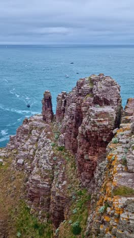 vertical rotating view over cap fréhel cliffs, boats in the ocean, and distant horizon in brittany, france