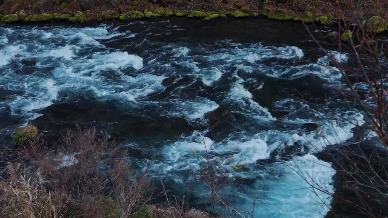 Close scenic view of a rushing river with powerful currents flowing across submerged rocks, creating whitewater, ripples and natural fluid motion.