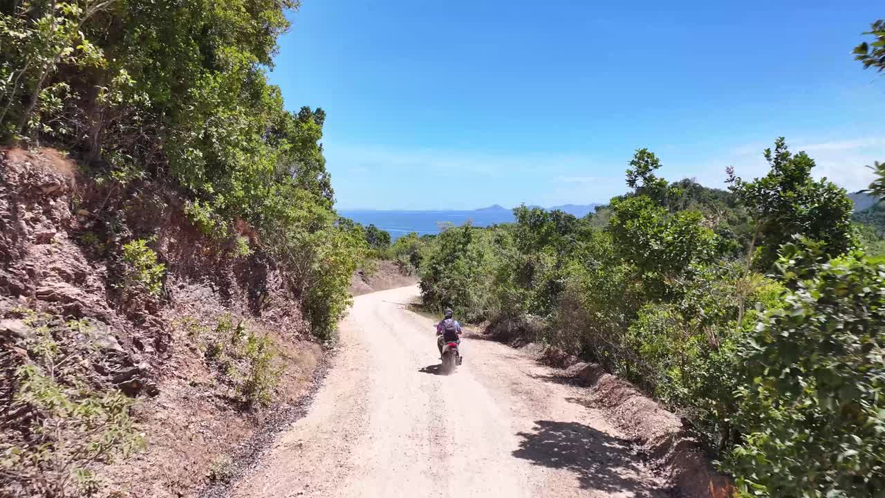 Man on motorbike on dirt road in Phillippines. Drone follow rider, tropical surroundings