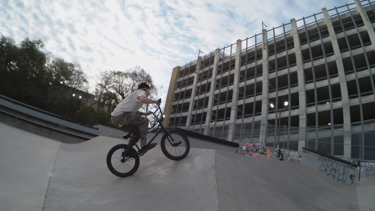 motociclista 360 giros en cámara lenta en el skatepark, beanie vuela lejos, 4k 800fps truco bmx al amanecer