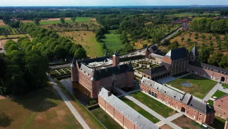 Aerial-circular-view-of-mansion-structure-with-greenery-in-Alden-Biesen-Castle-in-Belgium,-Germany-surrounded-by-beautiful-landscape-during-day