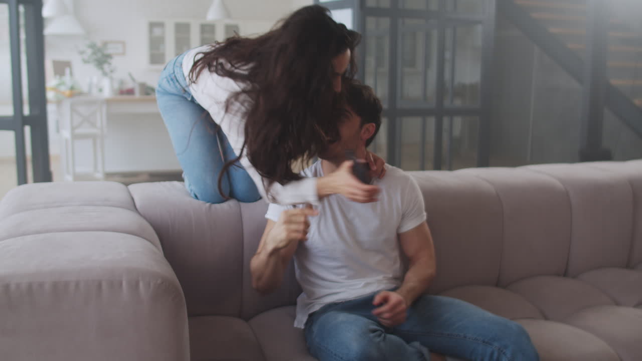 미소 짓는 여자가 집에서 소파에서 남자에게 달려갑니다.