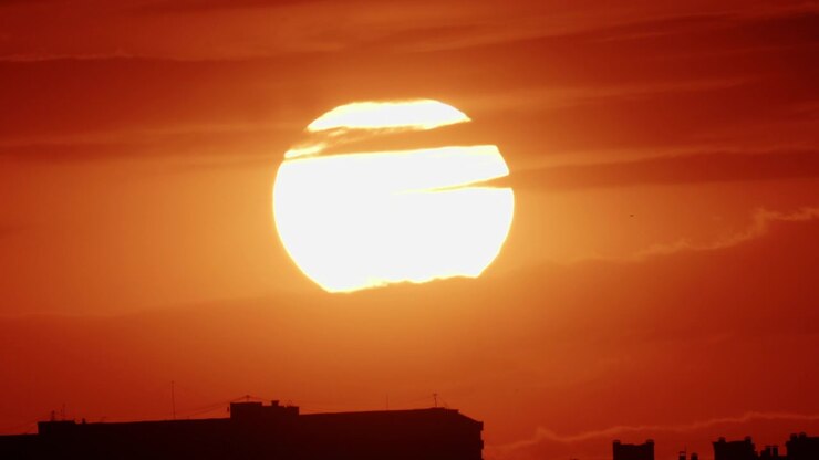 Golden sunset descending behind a dense urban skyline, silhouetting mid-rise residential buildings