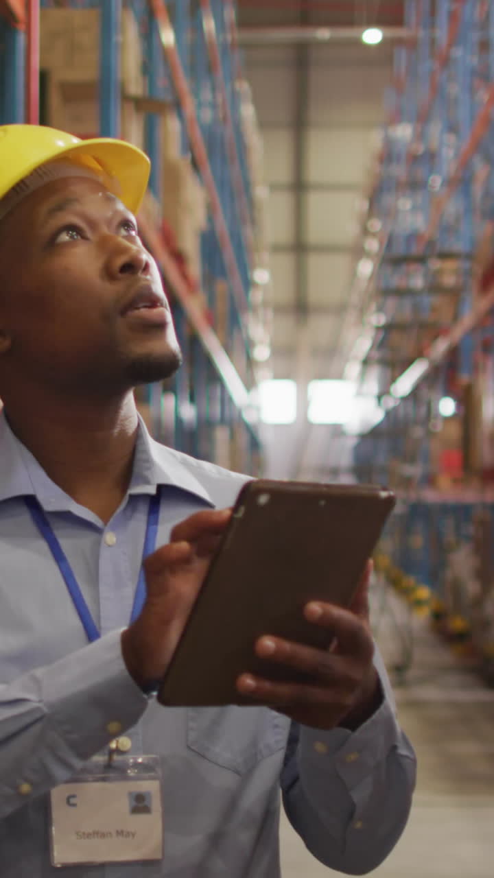 Lavoratore afroamericano con casco che usa un tablet in magazzino.