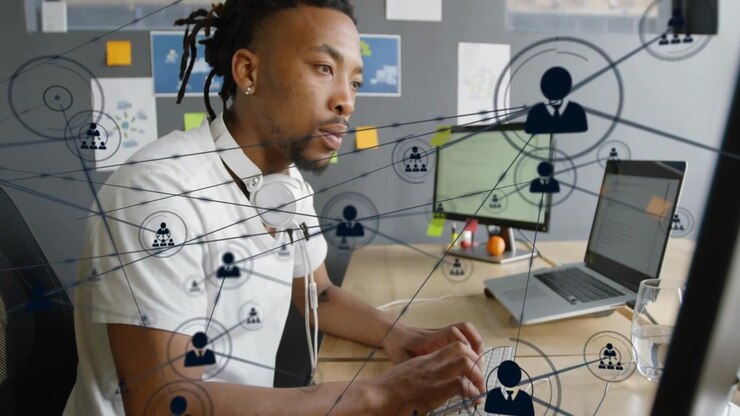 Man typing keyboard at desk, initiating user icons and lines growing across screens for tech demo