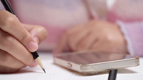 mujer escribe sus ingresos y gastos personales desde su teléfono en un cuaderno para el análisis financiero