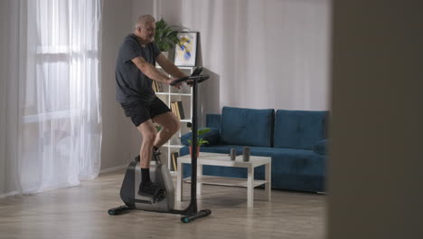 Entrenamiento-En-Casa-Con-Actividad-Deportiva-De-Bicicleta-Estacionaria-En-La-Mediana-Edad-El-Hombre-Está-Girando-Pedales-Entrenando-Respirando-Un-Estilo-De-Vida-Saludable