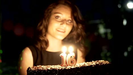 happy teen girl at 16 birthday party holding cake and burning candles smiling and having fun, handheld shot