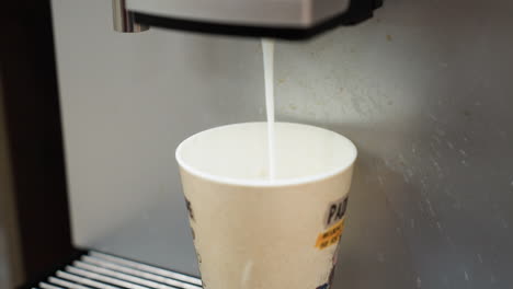 milk being poured into a coffee cup from a machine. focusing on the stream of milk filling the cup, capturing the precise moment of the coffee preparation process