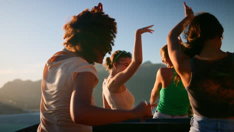 rear view of female friends standing up through sun roof of car dancing on road trip