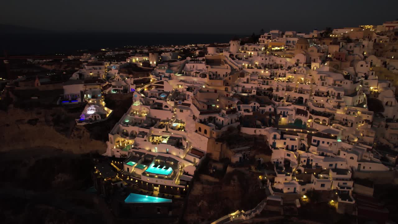 vista aérea de la isla de santorini por la noche, edificios blancos y piscinas iluminadas
