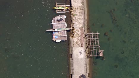 una fotografía aérea de un dron volando sobre un largo muelle de hormigón con barcos de pesca y cabañas de pescadores a ambos lados en balibayon, ciudad de surigao, filipinas