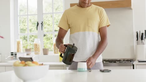 hombre biracial feliz haciendo café en una cocina brillante, cámara lenta