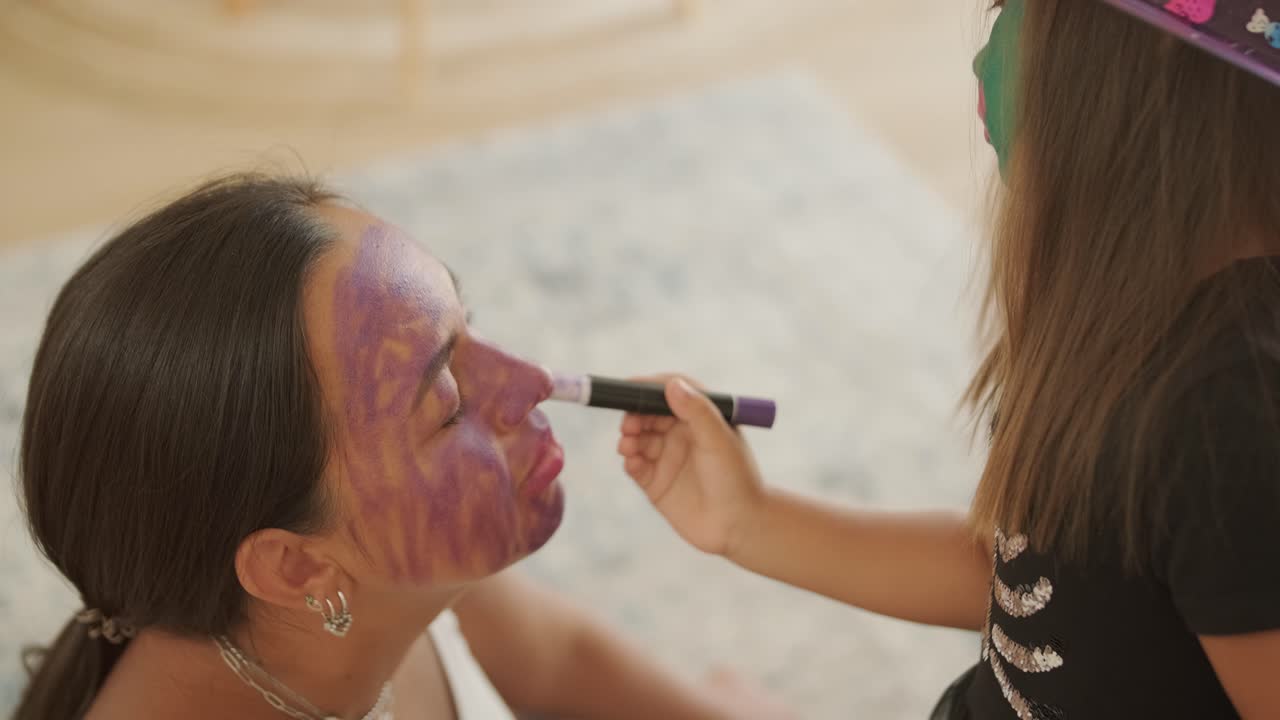 niña con sombrero de bruja aplicando maquillaje a su madre embarazada para halloween