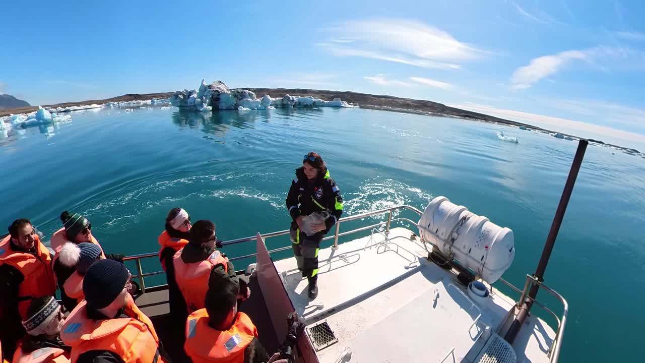 Woman on Glacier Lagoon boat tour holds up a chunk of glacial ice, sharing the breathtaking moment with her companions amidst Iceland's stunning natural beauty
