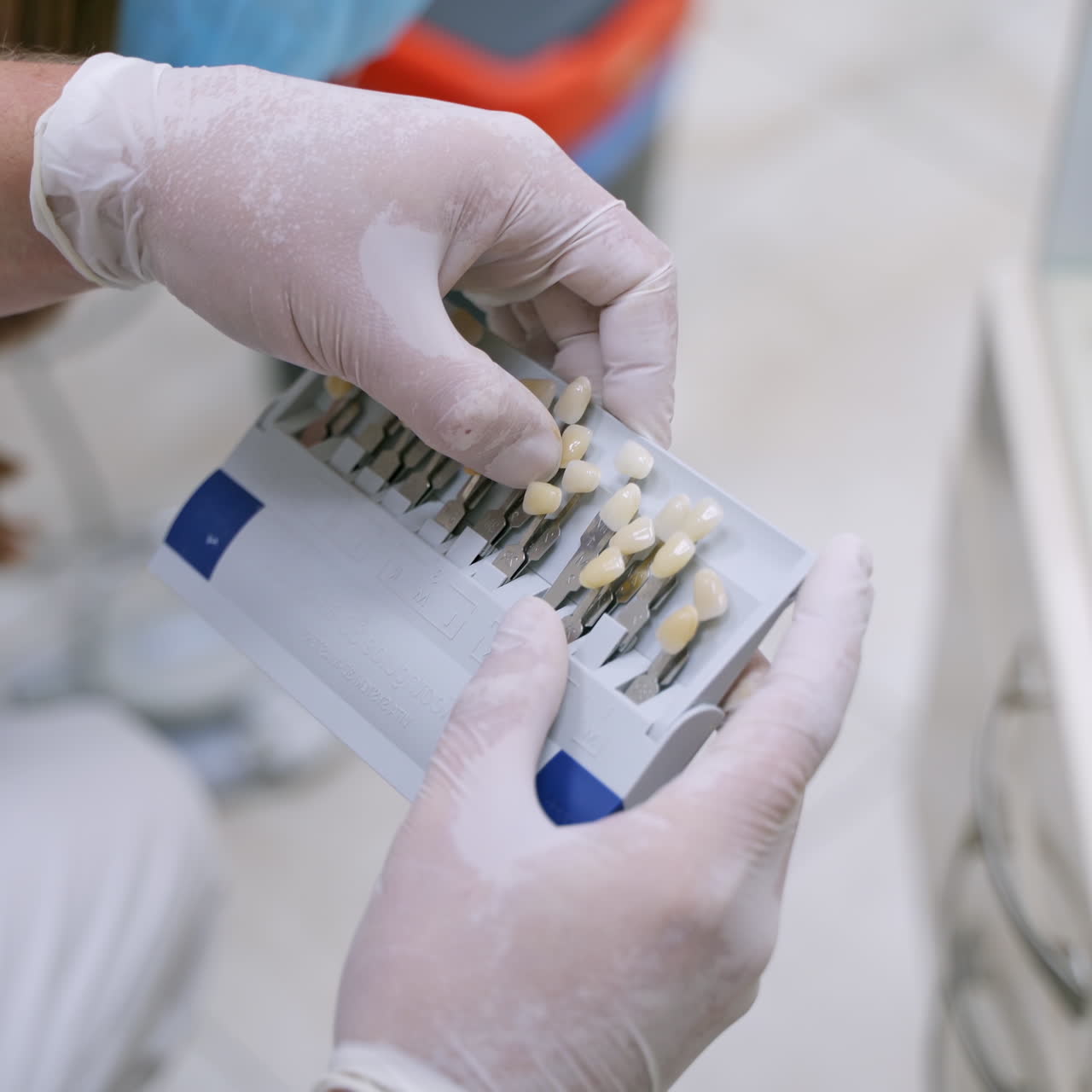 Stomatologist holding artificial teeth. Dentist in gloves selects a color for the patient to create a prosthesis. Progress of dental implantology.