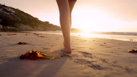 woman walking barefoot on beach at sunset