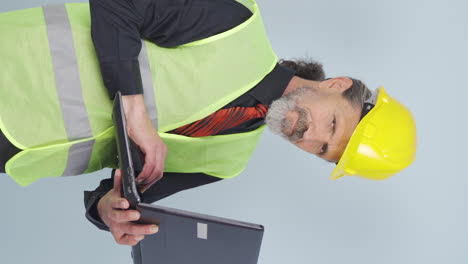 vertical video of old engineer holding laptop laughing at camera.