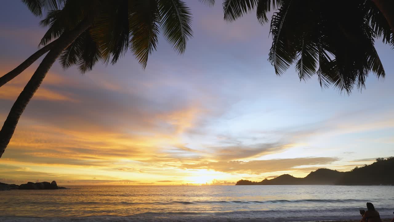 Sunset at takamaka beach woman on sitting on the beach taking pictures, Mahe, Seychelles.