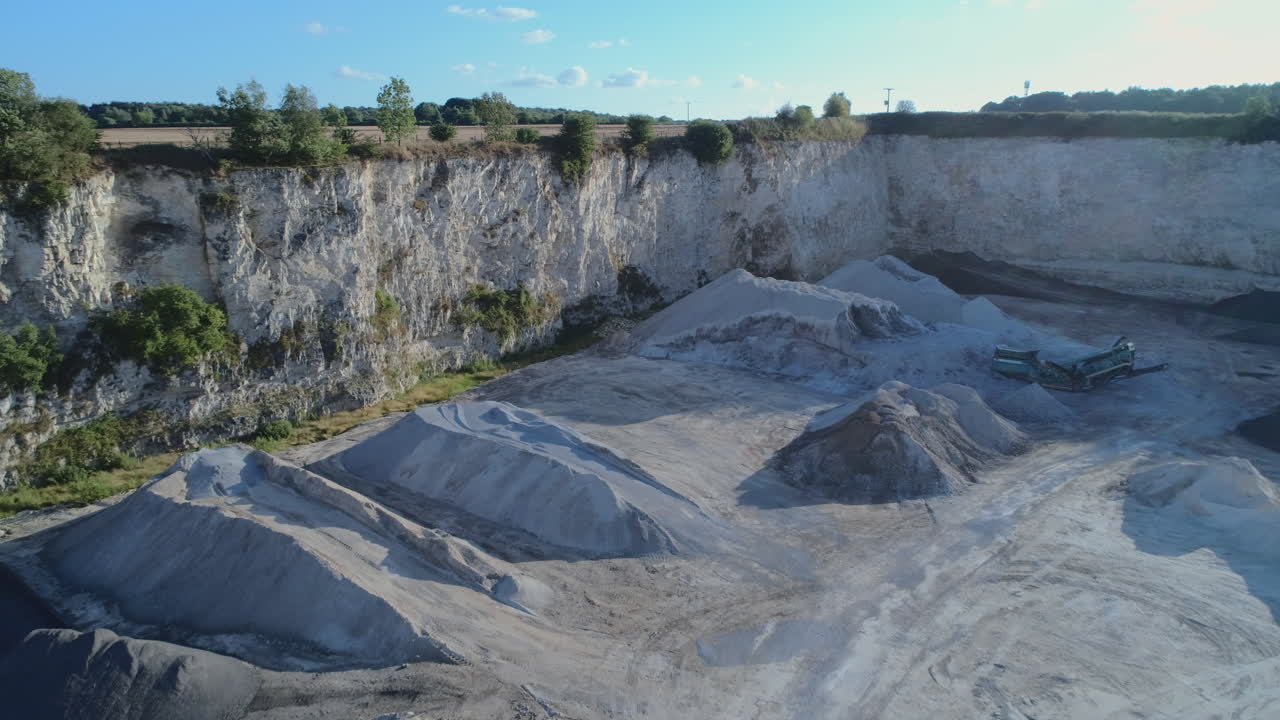 Drone Shot of Openpit Limestone Quarry with Mounds of Gravel and White Limestone Cliffs with Small Trees on Edges on Sunny Day Yorkshire UK