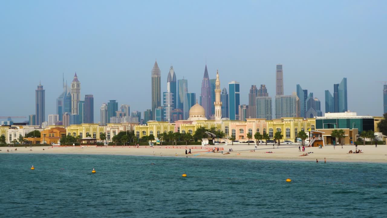 전경에 해변과 모스크가 있는 두바이 스카이라인의 부드러운 풀아웃 샷