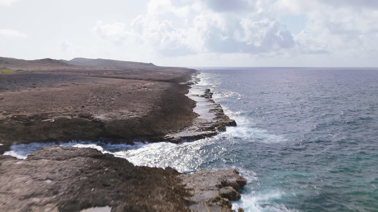 Aerial dolly along Curacao’s rugged northern coastline with waves crashing against the rocky cliffs and open ocean and tide pools gathering in low areas