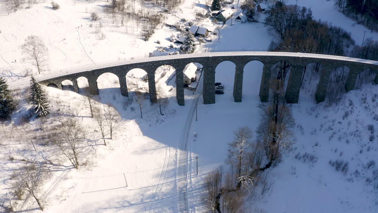 каменный железнодорожный виадук, возвышающийся над маленькой деревней, заснеженный
