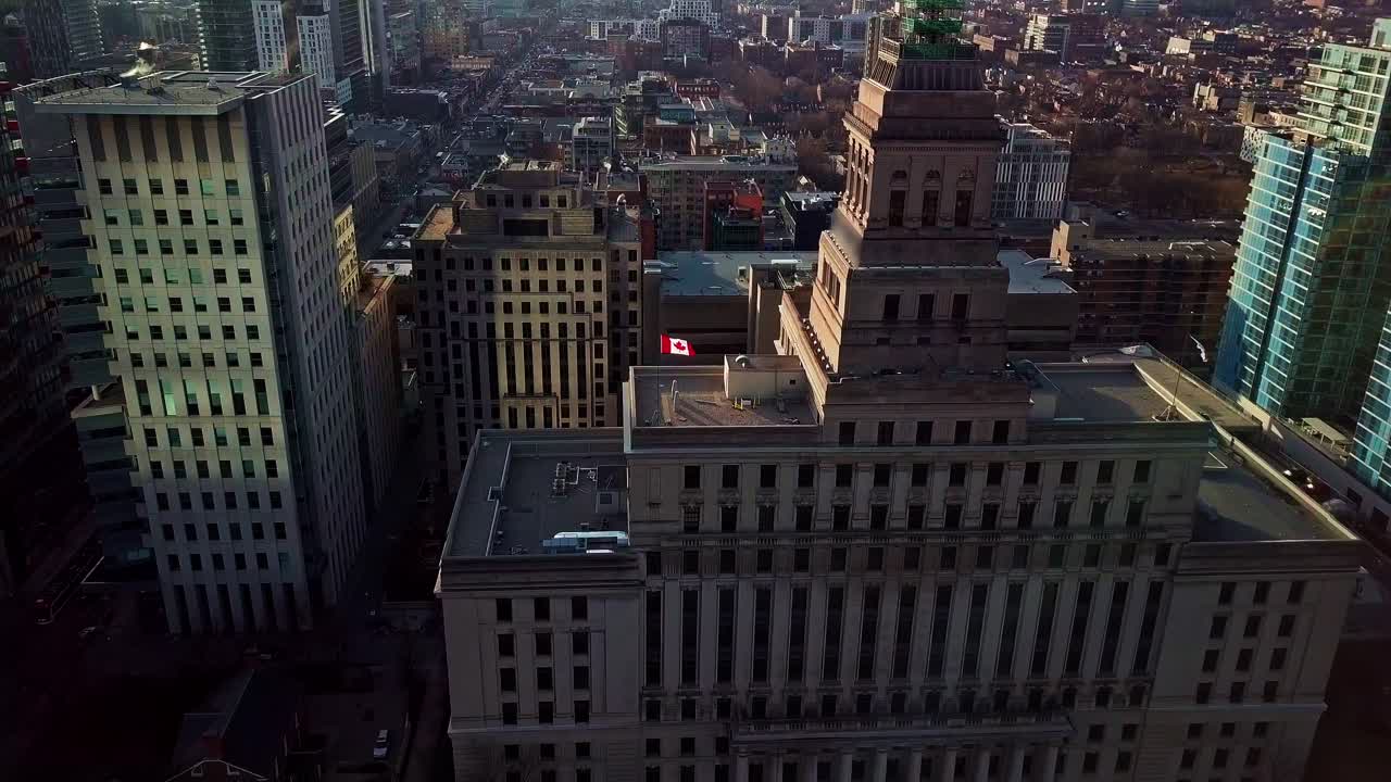 Stunning Drone View of Canadian Flag on a Historic Building in Toronto, Wide Aerial Dolly In Tilt Down to Overhead with Beautiful Lens Flare and Tall Downtown Skyscrapers near Sunset