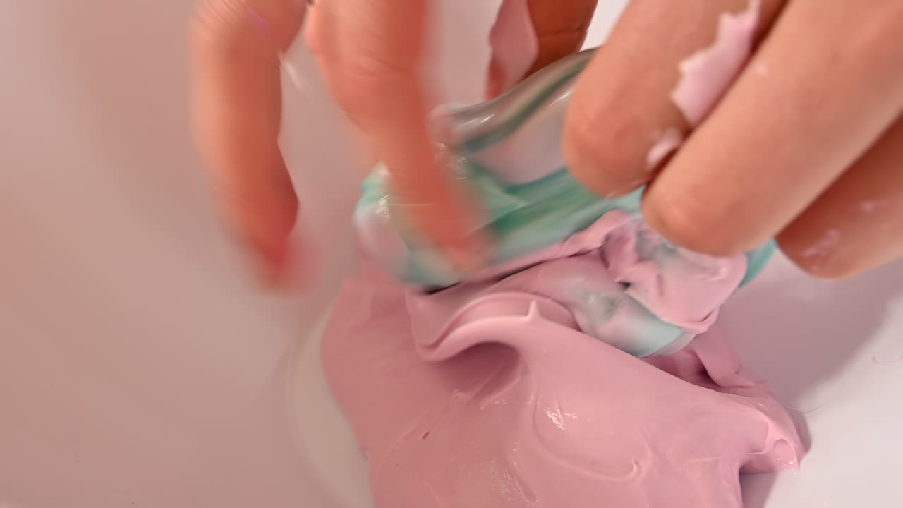 Beyaz bir arka planda turkuaz ve pembe slime karıştıran kadın