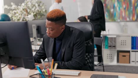 un homme élégant travaillant dans un bureau un garçon est assis derrière un bureau devant un ordinateur, vérifiant l'exactitude des documents papier et électroniques, entrant des données dans le système en tapant des doigts sur le clavier