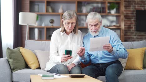 senior family couple, gray haired old man and woman pay for services enter data documents using application mobile smartphone