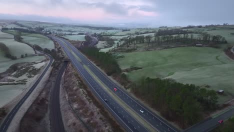 passenger train moving alongside quiet m6 motorway at dawn in winter