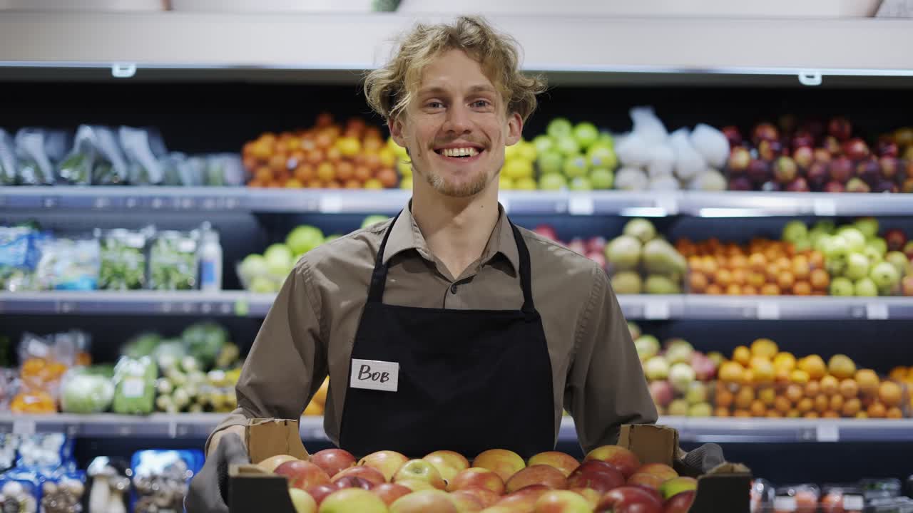 trabajador feliz en un delantal negro está sosteniendo una caja de manzanas. trabajo en la tienda. días laborables. comida saludable