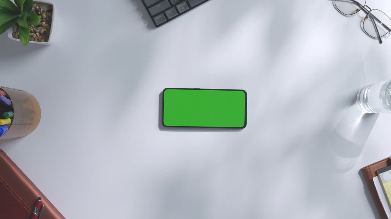 vista de arriba hacia abajo de una computadora portátil con pantalla verde simulada pantalla chromakey en un escritorio de oficina de madera al lado de la libreta con bolígrafos, gafas y un vaso de agua.