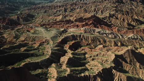 Cinematic-aerial-shot-of-Fairy-Tale-Canyon-and-Issyk-Kul-Lake-in-Karakol,-Kyrgyzstan,-starting-downward-then-tilting-up-to-reveal-the-water