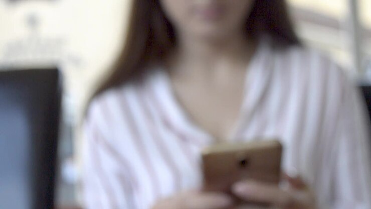 Detailed view of pizza with ham and sweetcorn with a girl sitting behind and playing with her phone, TITL UP