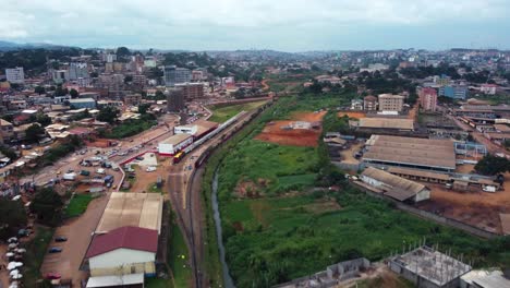 vista aérea que se eleva sobre un río, siguiendo el ferrocarril de la ciudad, en nublado yaounde, camerún