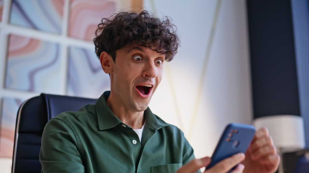 Man with curly hair using smartphone and reacting with surprise