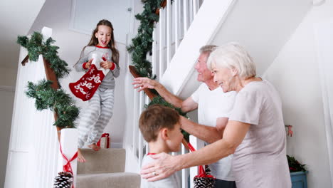 abuelos saludando nietos emocionados con pijama corriendo por las escaleras sosteniendo medias en la mañana de navidad
